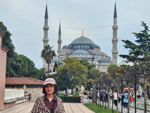 Traveller stands before Istanbul’s Blue Mosque with minarets rising against pale sky and trees.