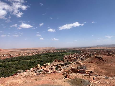 Sweeping aerial view over a green oasis valley surrounded by reddish desert hills and scattered villages.
