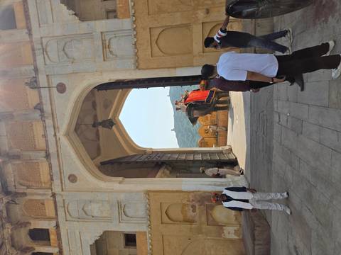 Elephant carrying tourists exits a massive arched gate at Amber Fort while visitors watch.
