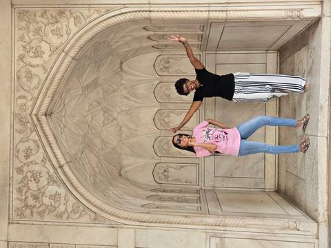 Two friends strike playful poses inside a white-marble alcove with floral carvings.