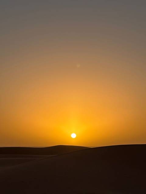 Minimalist image of a glowing orange sun just above the horizon in a clear sky.