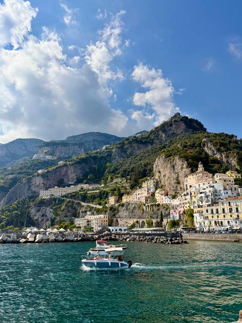 Colorful Amalfi Coast village clings to steep cliffs beneath towering mountains.
