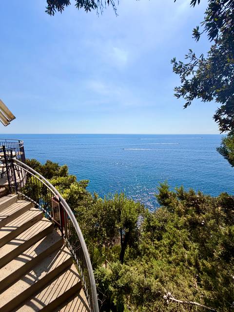 Calm open sea view from a terrace railing under a cloudless blue sky.