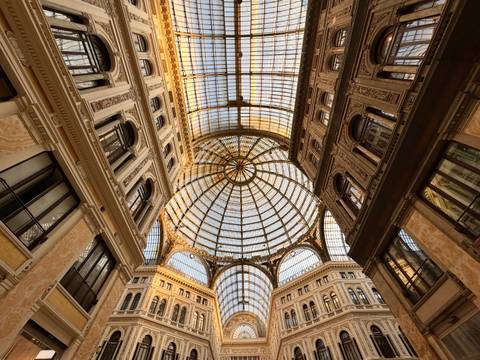 Grand glass-domed arcade ceiling of a 19th-century shopping gallery lit by warm light.