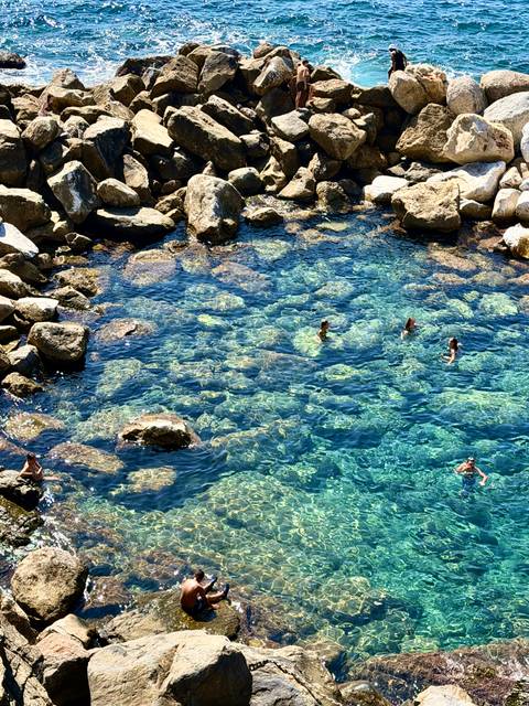 Clear turquoise cove with swimmers enjoying the water above sun-lit rock formations