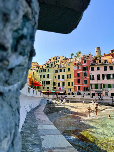 Colorful seaside buildings of Cinque Terre rising above a small beach with people and umbrellas