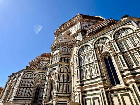 Ornate marble façade and dome of Florence’s Duomo under a deep blue sky