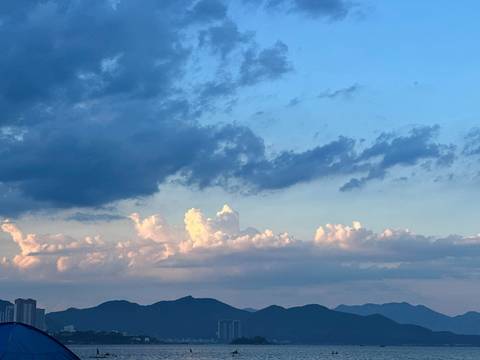 Evening sky with dramatic clouds over distant mountains and a sliver of city skyline.