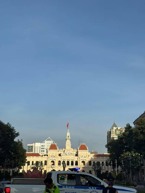 Wide view of a clear blue sky above city rooftops with a national flag atop a tall building.