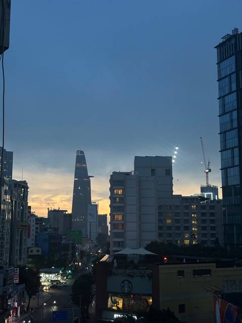 City skyline at dusk with the distinctive Bitexco Financial Tower and construction cranes silhouetted.