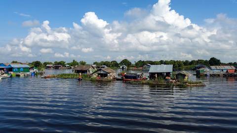 Stilted floating village houses and fishing boats on the calm waters of Tonle Sap Lake beneath a bright sky.