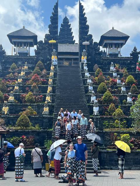 Large stairway of an ornate Balinese temple with a tour group at the base and colourful foliage on the tiers.