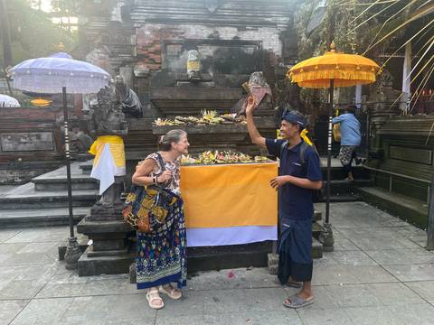 Travellers interact with a Balinese guide beside an offering table inside a temple courtyard.