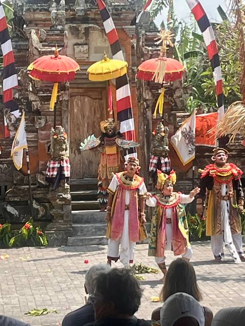 Balinese dancers in colourful traditional costumes perform on an outdoor temple stage.