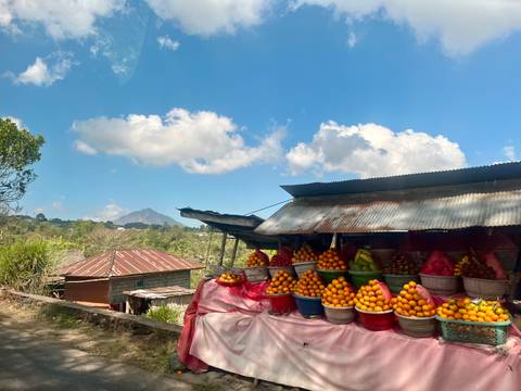 Roadside fruit stall stacked with baskets of oranges against a backdrop of a distant volcano.