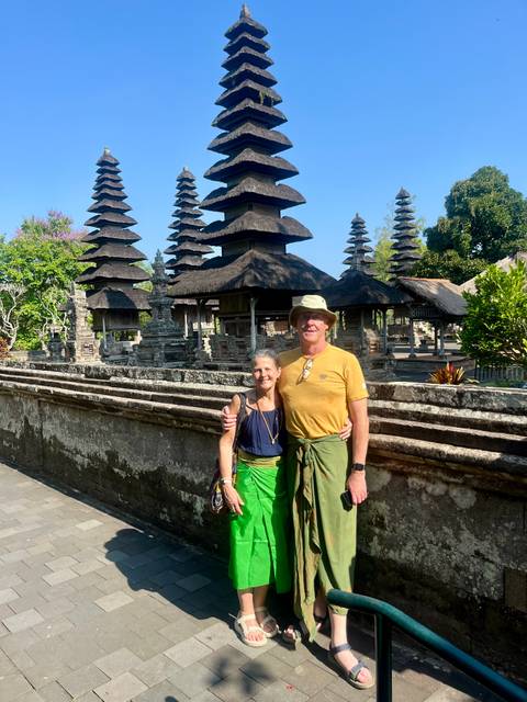 Couple dressed in sarongs stand by multi-tiered pagoda shrines of a royal temple complex.