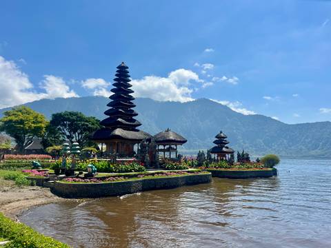 Iconic lakeside Ulun Danu Beratan temple with flower gardens and mountain backdrop under blue sky.