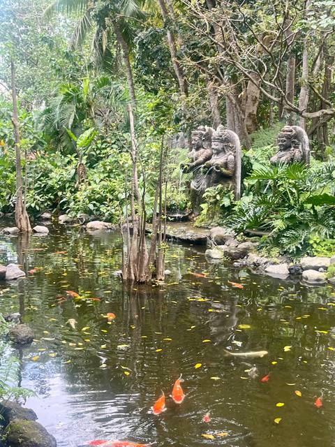 Serene koi pond surrounded by lush tropical plants and stone goddess statues.