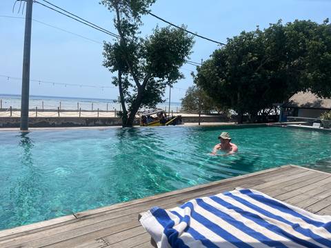 Traveller enjoys an infinity pool overlooking a calm beach and anchored boat.
