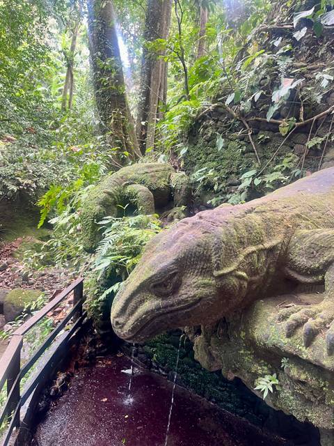 Moss-covered reptile sculptures blend into dense forest foliage.