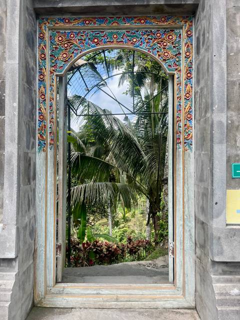 Decorative doorway painted with floral motifs opening to tropical palms outside.