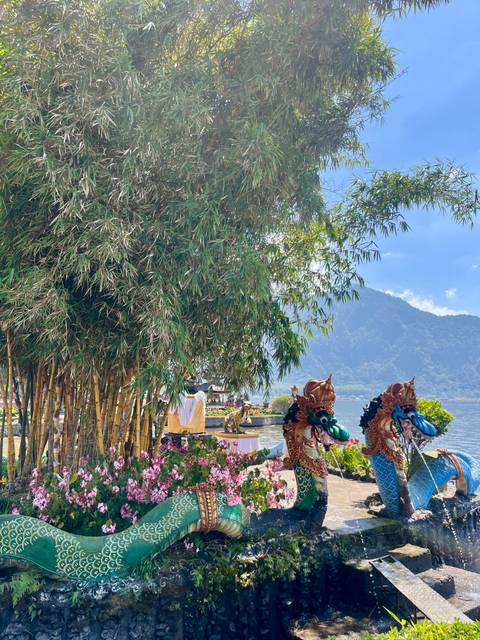 Bamboo grove, ceremonial statues and lake with mountains beyond under clear skies.