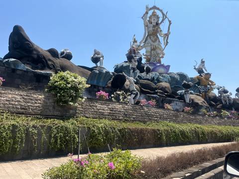 Massive mythological statue ensemble with flowers against a bright blue sky.