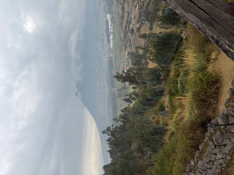 Misty valley view of a dormant volcano rising above patchwork farmland under gray skies.