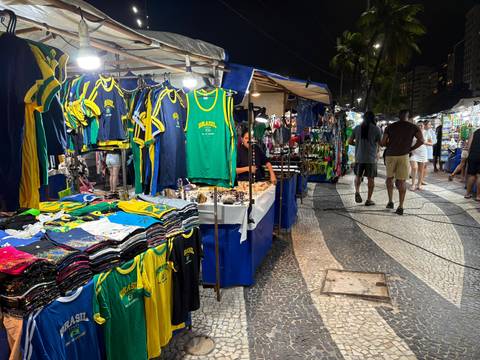 Bustling night market stalls selling colourful Brazil jerseys and souvenirs along a tiled promenade.