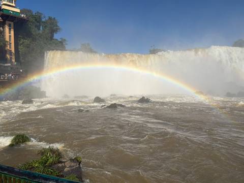 Vibrant rainbow arches over the rushing brown waters at the base of Iguazu Falls.