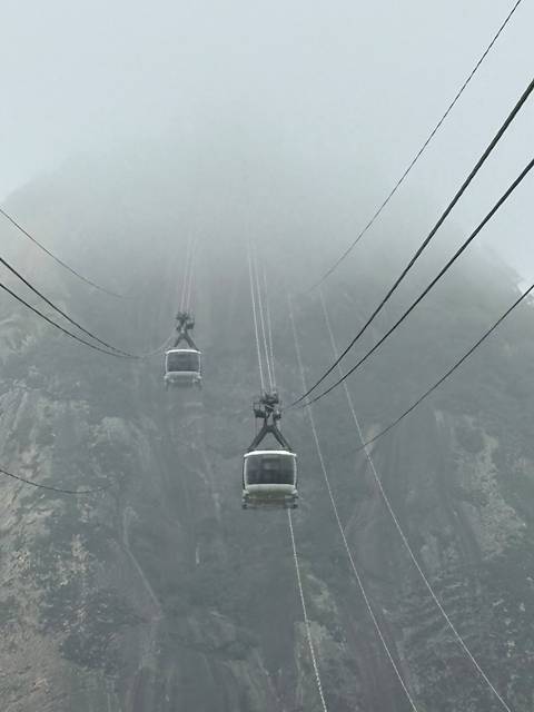 Cable cars disappear into thick fog on a steep granite mountain face.
