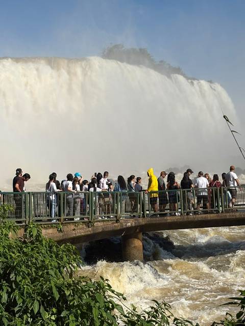 Tour group stands on a wet walkway amid dense mist from Iguazu Falls.