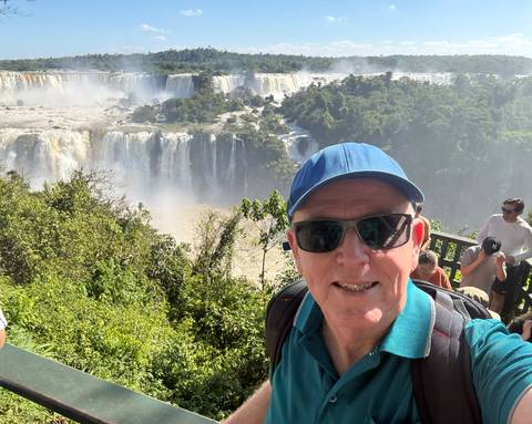 Selfie of a traveller in sunglasses overlooking Iguazu Falls from a forested viewpoint.