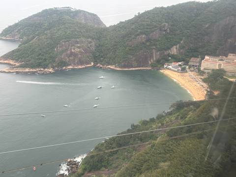 Aerial view through cable-car window of a small beach cove and boats below rocky cliffs.