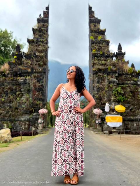 Smiling woman in sundress posing between the iconic split stone gates with misty mountains behind.