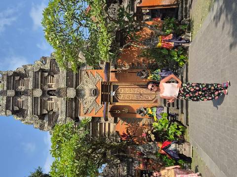 Traveler strikes a pose in front of an ornate Balinese temple gate flanked by guardian statues.