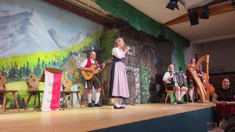 Traditional alpine music performance on stage with singers, guitar, accordion and harp.