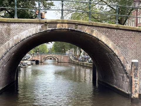 View through a brick arch bridge over a calm Amsterdam canal with more bridges in the distance.