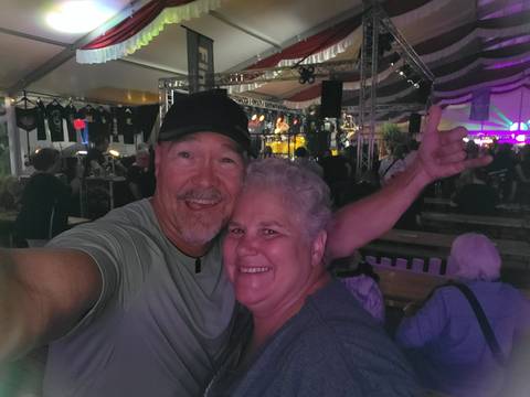 Low-light selfie of a couple inside a lively festival tent with stage lights in the background.