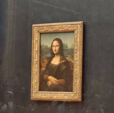 Photo of the Mona Lisa painting behind protective glass at the Louvre.
