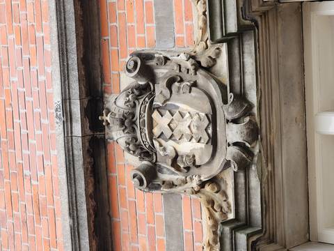 Stone coat of arms with triple X crest mounted on a red-brick Amsterdam building.