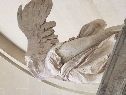 Marble statue of the Winged Victory of Samothrace viewed from below inside the Louvre.