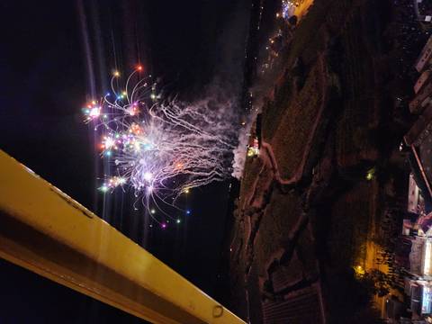 Multi-colored fireworks launching into the sky above a dark hillside at night.