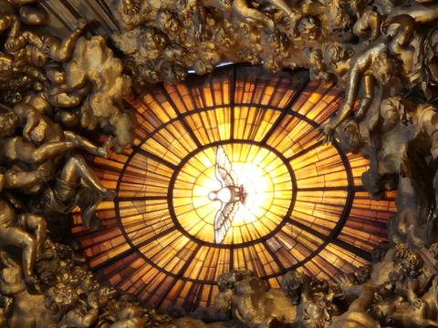 Radiant golden stained-glass window featuring a white dove surrounded by dramatic baroque sculpture inside a grand basilica.