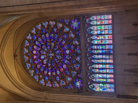 Vibrant rose window and rows of colourful stained-glass panels in a towering Gothic cathedral nave.
