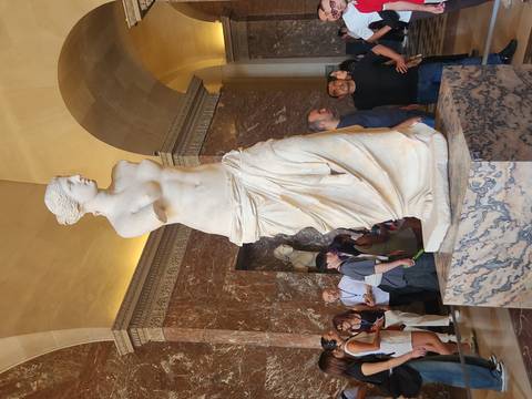 Marble Venus de Milo statue displayed in an ornate hall as visitors admire the masterpiece.