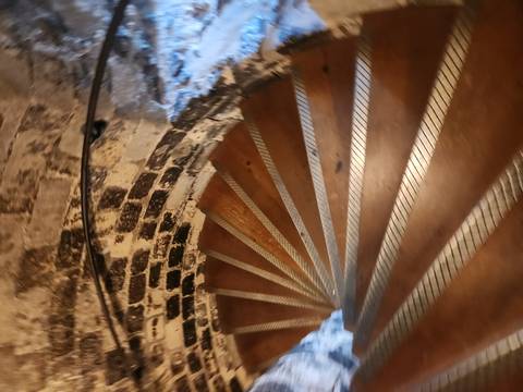 Blurred view down a narrow wooden spiral staircase within a stone tower.