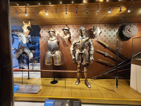Display of medieval and renaissance suits of armour, helmets and polearms in a museum gallery.