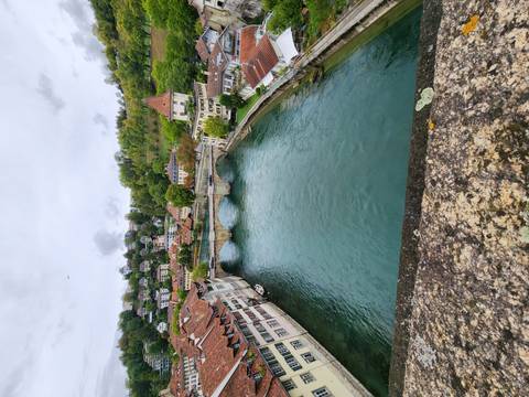 Elevated view of a stone bridge crossing a calm turquoise river flanked by tiled rooftops and green hills.