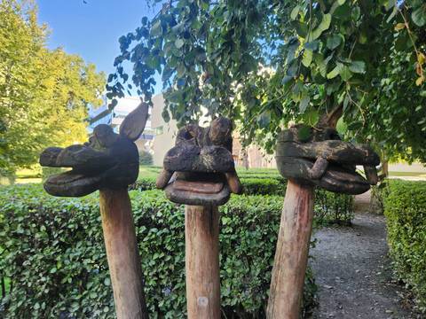 Three carved wooden animal heads mounted on posts in a leafy park setting.